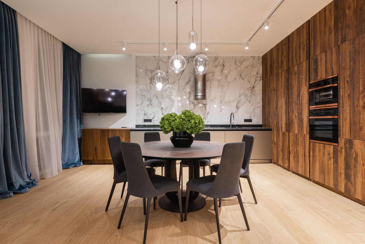 Interior of modern apartment with chairs near round table with vase with green plants near kitchen counter and curtains near TV
