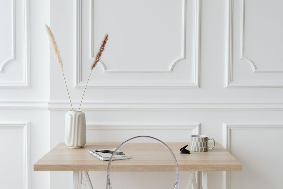 Minimalist desk setup with a ceramic vase, dried grass, mug, and notebook in a modern interior.