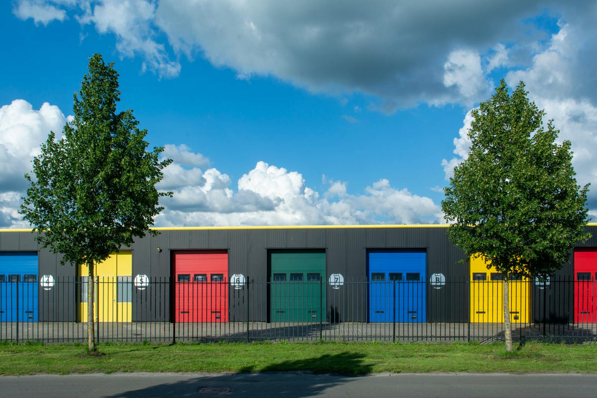 Vibrant garage doors in different colors with bright sky and clouds above, enclosed by iron gates.
