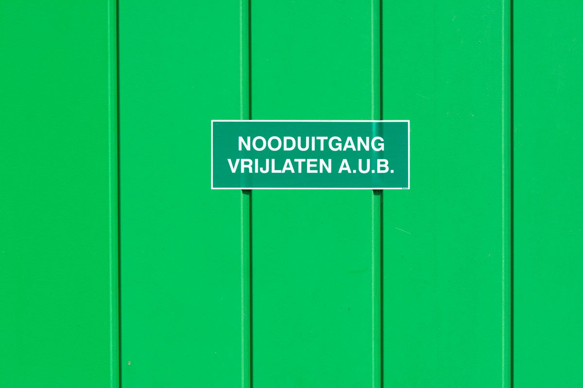 A green metal wall featuring an emergency exit sign in Dutch. Perfect for safety-themed graphics.