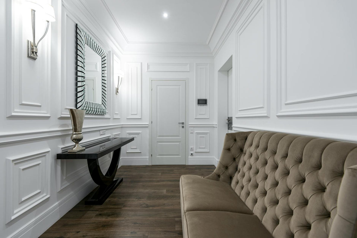Luxurious white interior featuring a modern tufted sofa and classic wall paneling.