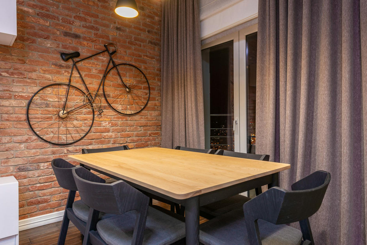 Bicycle on rough wall against table and chairs under shiny lamp in modern room at home