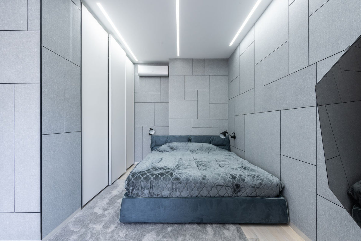 Interior of light modern bedroom with gray bed on carpet near lamps on wall and TV