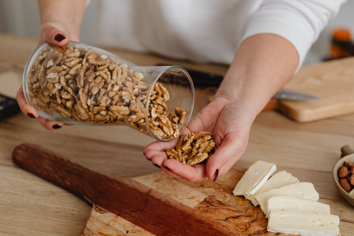 Person pouring walnuts onto a board with sliced cheese, combining fresh ingredients.
