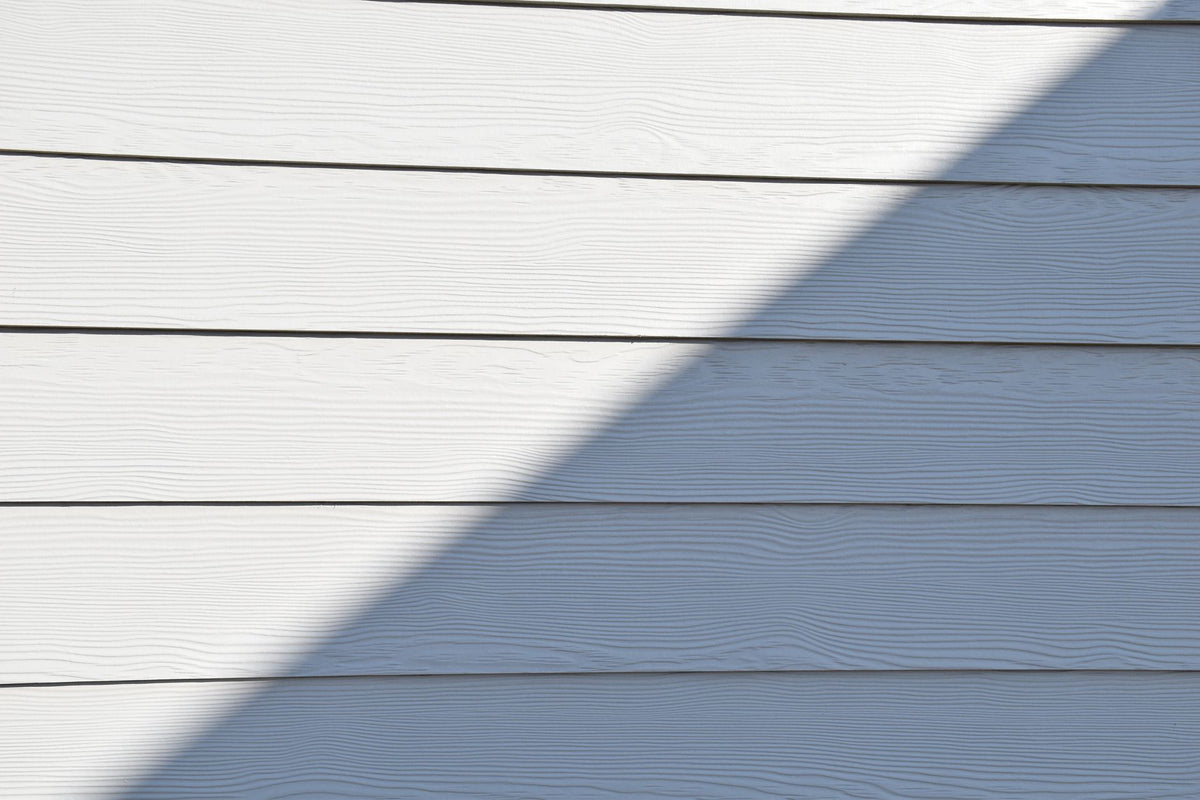 Close-up of a white wooden wall featuring a bold diagonal shadow.
