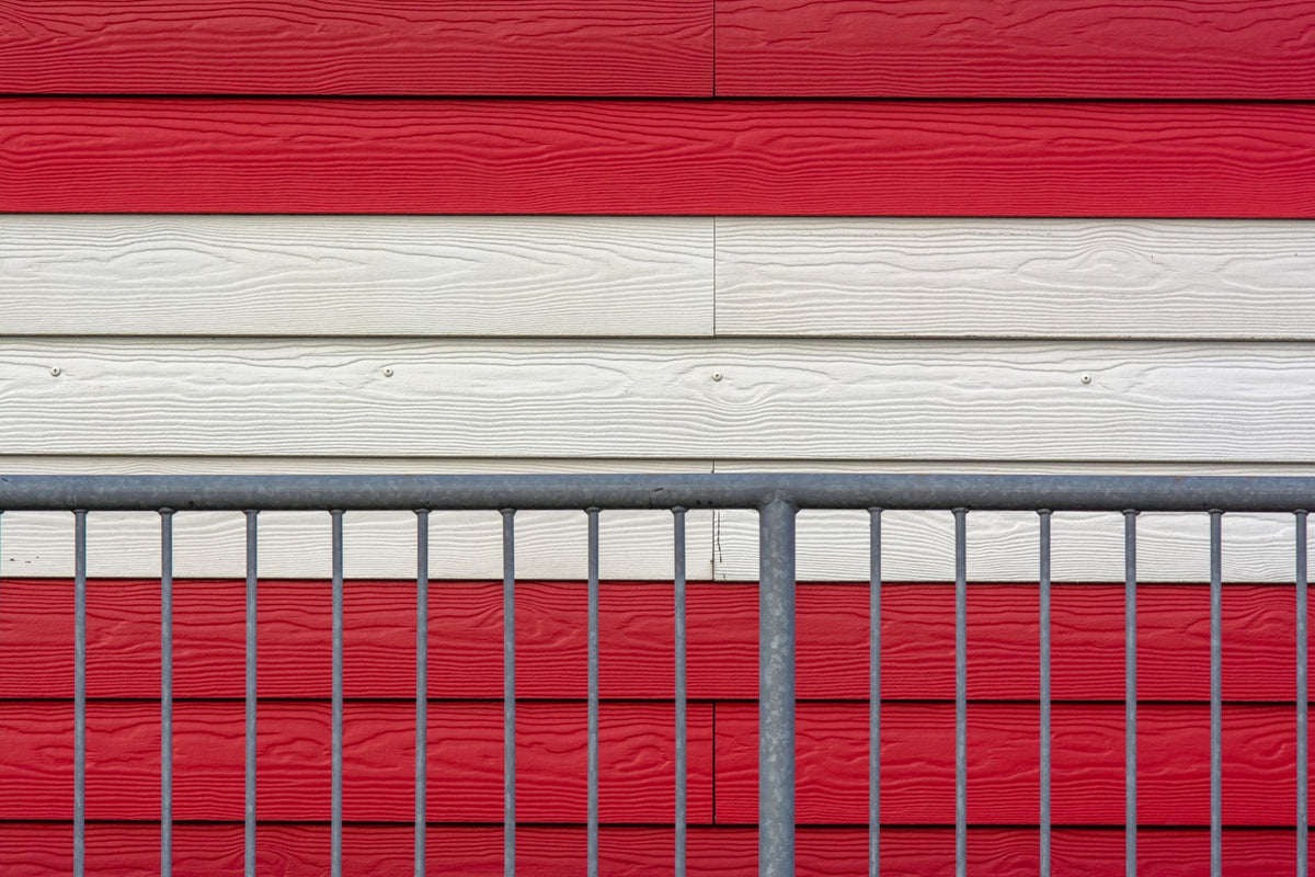 Close-up of a red and white striped wooden wall with a metal fence in front.