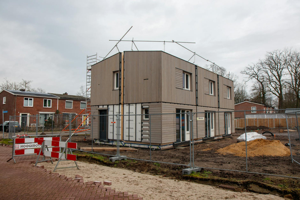 A modern house under construction with scaffolding, fences, and construction signs on a cloudy day.