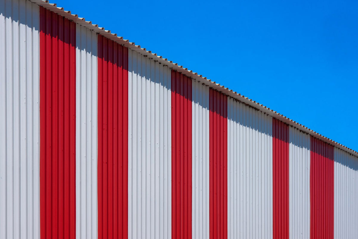 A bold red and white striped industrial building contrasted against a clear blue sky.